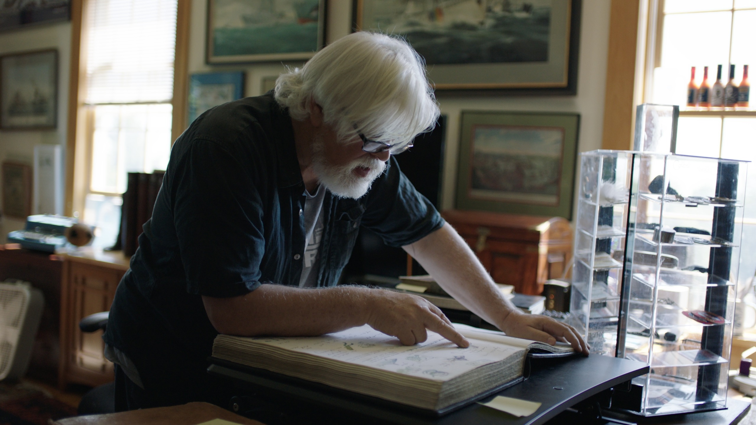 An older man with white hair and a beard is engrossed in a large book on a desk, his glasses glinting as he points at the pages. The room, filled with framed pictures, is softly lit by sunlight streaming through the window, casting gentle shadows reminiscent of Watson's tranquil studies.