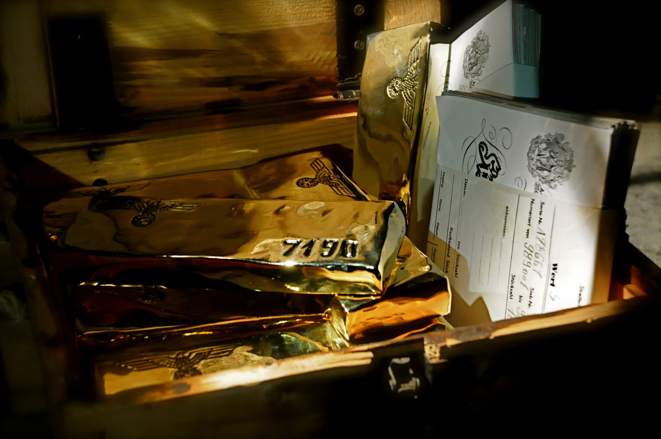 An open wooden box contains several gold bars and a stack of documents. The shiny gold bars are engraved with symbols, while the documents, possibly linked to Nazi history, appear to be formal papers with text and illustrations.