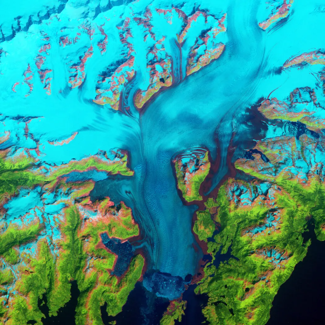 Satellite image of a vibrant landscape with glacial blue ice, intricate patterns of white snow, and lush green land. Deep blue water bodies surround the area, creating a striking contrast.