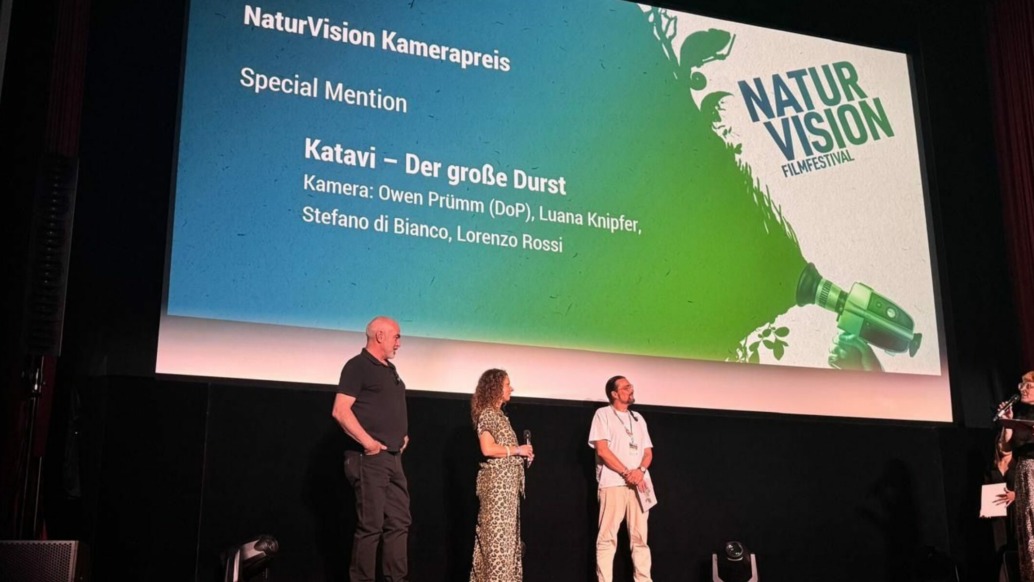 Four people stand on stage at an awards ceremony. Behind them, a large screen displays NaturVision Kamerapreis and Katavi – Der große Durst, listing contributors and featuring the NaturVision Filmfestival logo for the prestigious awards event.