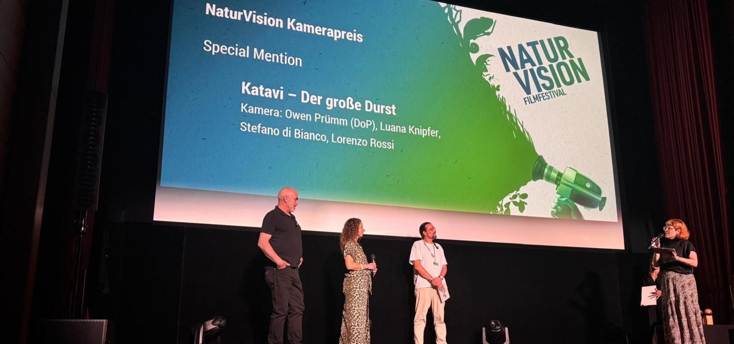 Four people stand on stage at an awards ceremony. Behind them, a large screen displays NaturVision Kamerapreis and Katavi – Der große Durst, listing contributors and featuring the NaturVision Filmfestival logo for the prestigious awards event.