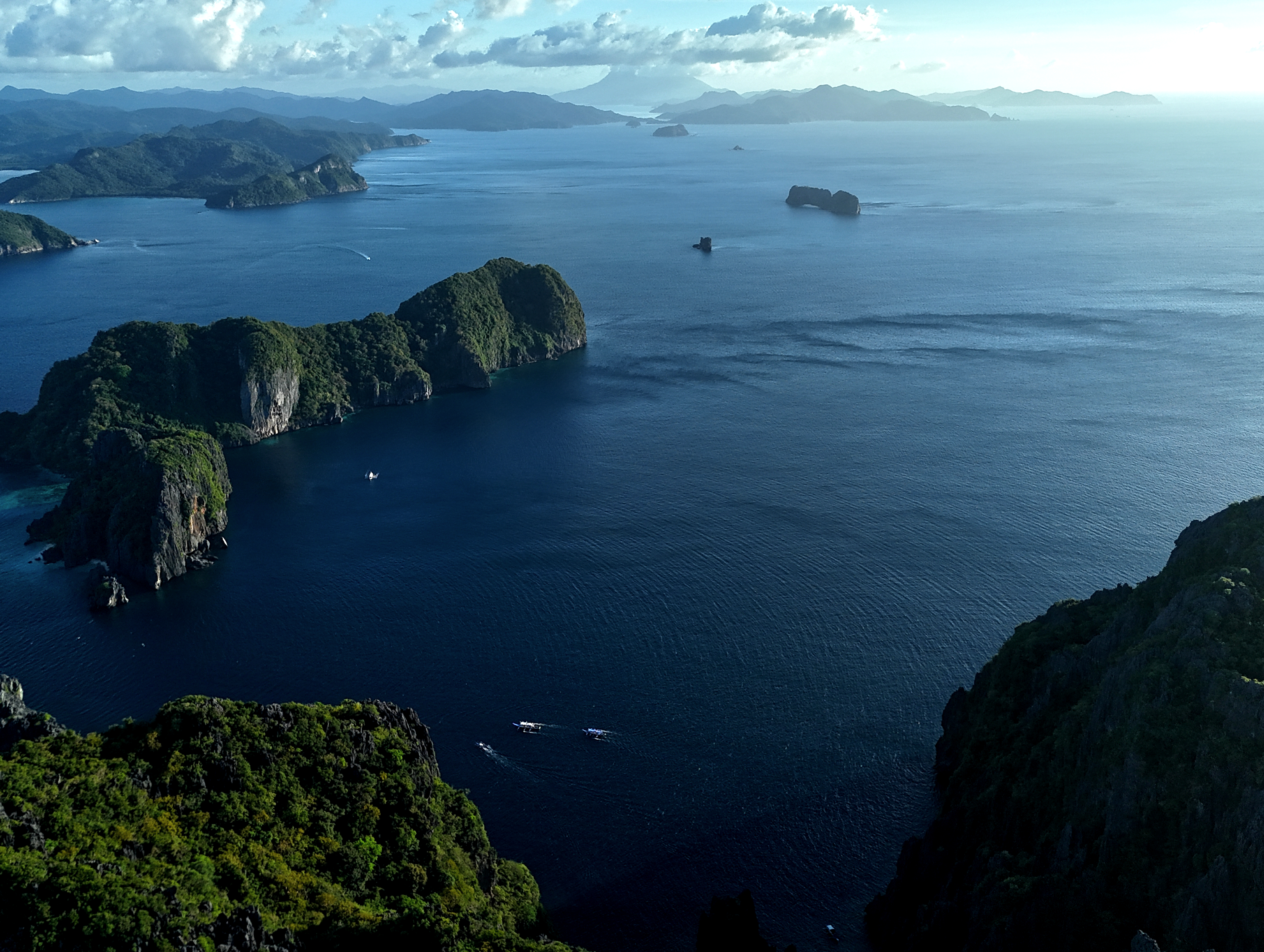 Aerial view of lush limestone islands and small boats dotting the deep blue waters of El Nido, Palawan, a true example of the wild Philippines.