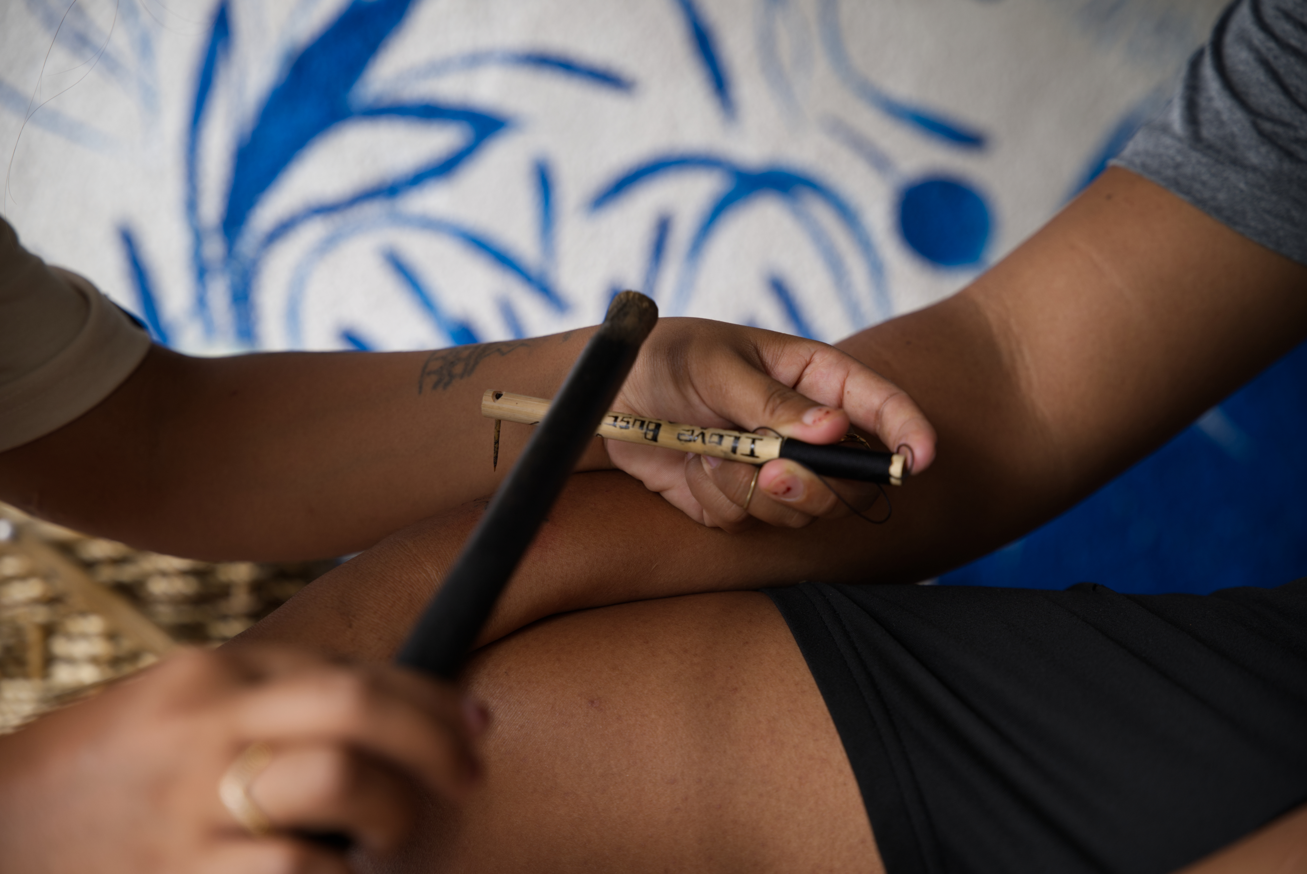 A person uses a traditional bamboo tapping tool to hand-tap a tattoo onto another person’s arm in the wild Philippines.